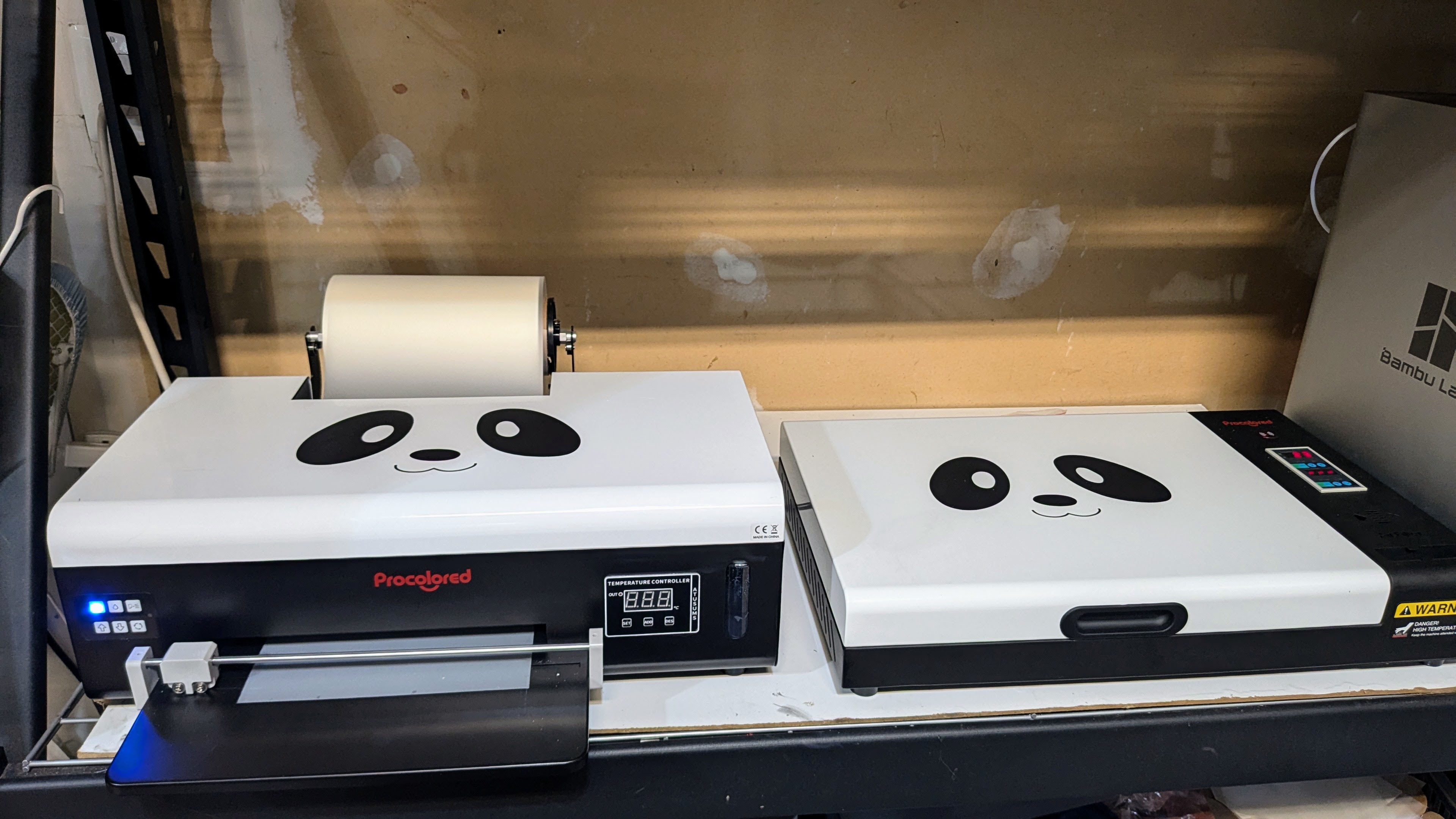 A black and white printer with a panda face on top. A thin version seats next to it on a black shelf.