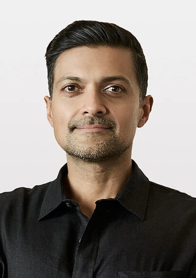 Portrait of a man with short dark hair and a trimmed beard wearing a black shirt against a plain background.