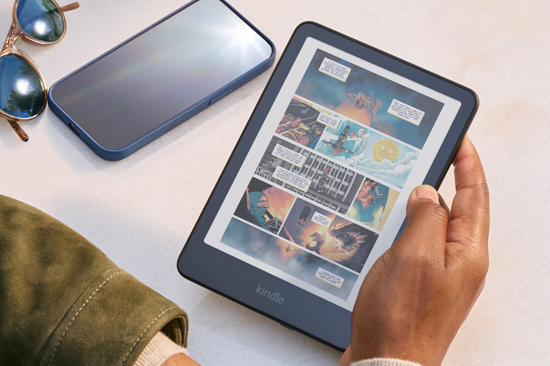 Amazon's Kindle Colorsoft (16GB) being held with a smartphone and sunglasses next to it.